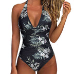ZOFIA ATELIER black one-piece swimsuit with white floral and green leaf print, deep V-neck, halter straps, and ruched sides.