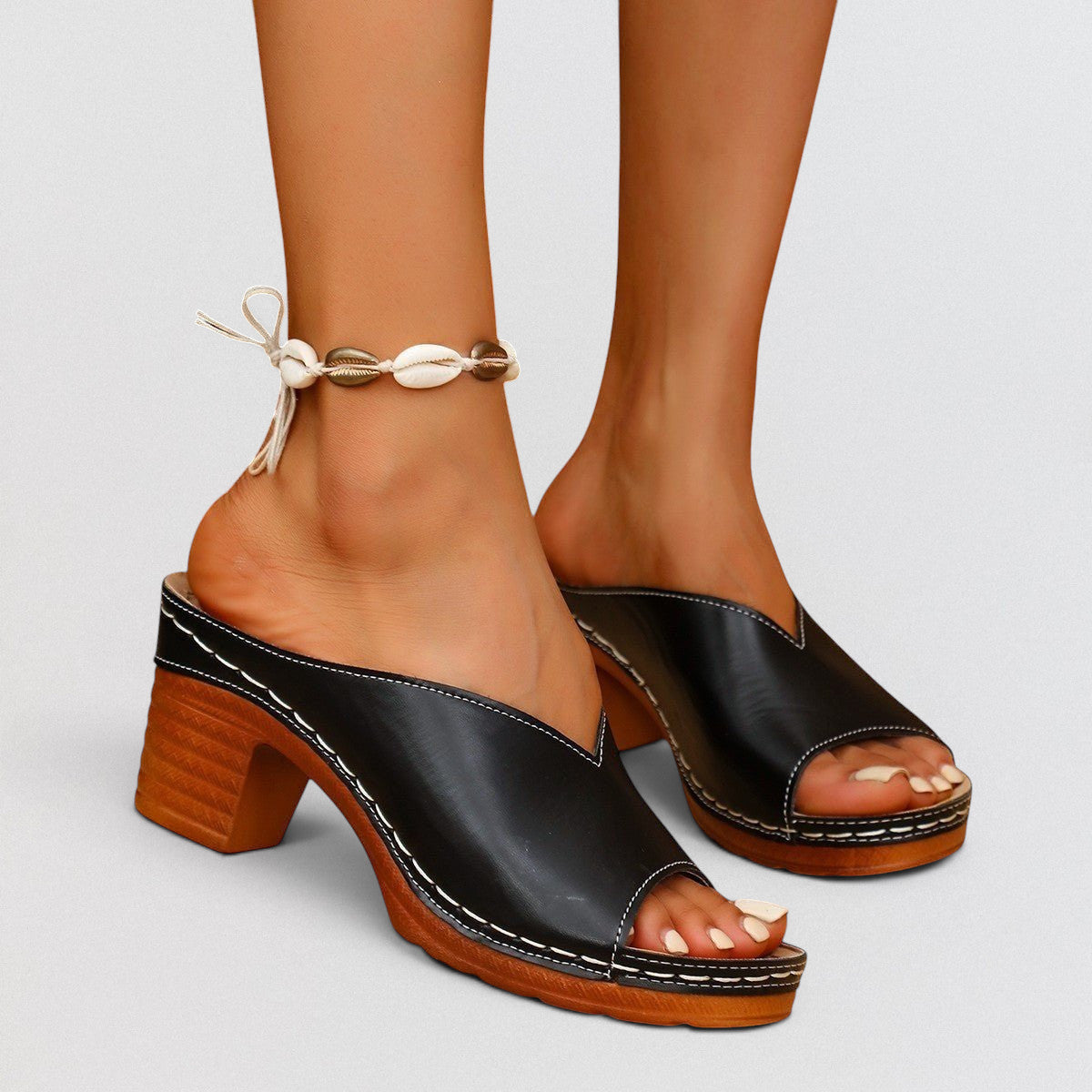 ZOFIA ATELIER black leather open-toe block heel slide slippers with white stitching and a seashell anklet.