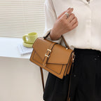 ZOFIA ATELIER Ewerina crossbody bag in brown PU leather with gold buckle detail. Features a structured design and a contrast color lock.