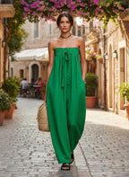 ZOFIA ATELIER green ruched strapless polyester jumpsuit with a tie waist and wide legs, worn by a model on a cobblestone street.