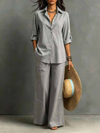ZOFIA ATELIER grey cotton resort set with full-length pants and regular sleeve shirt. Model holds a wide-brimmed hat.