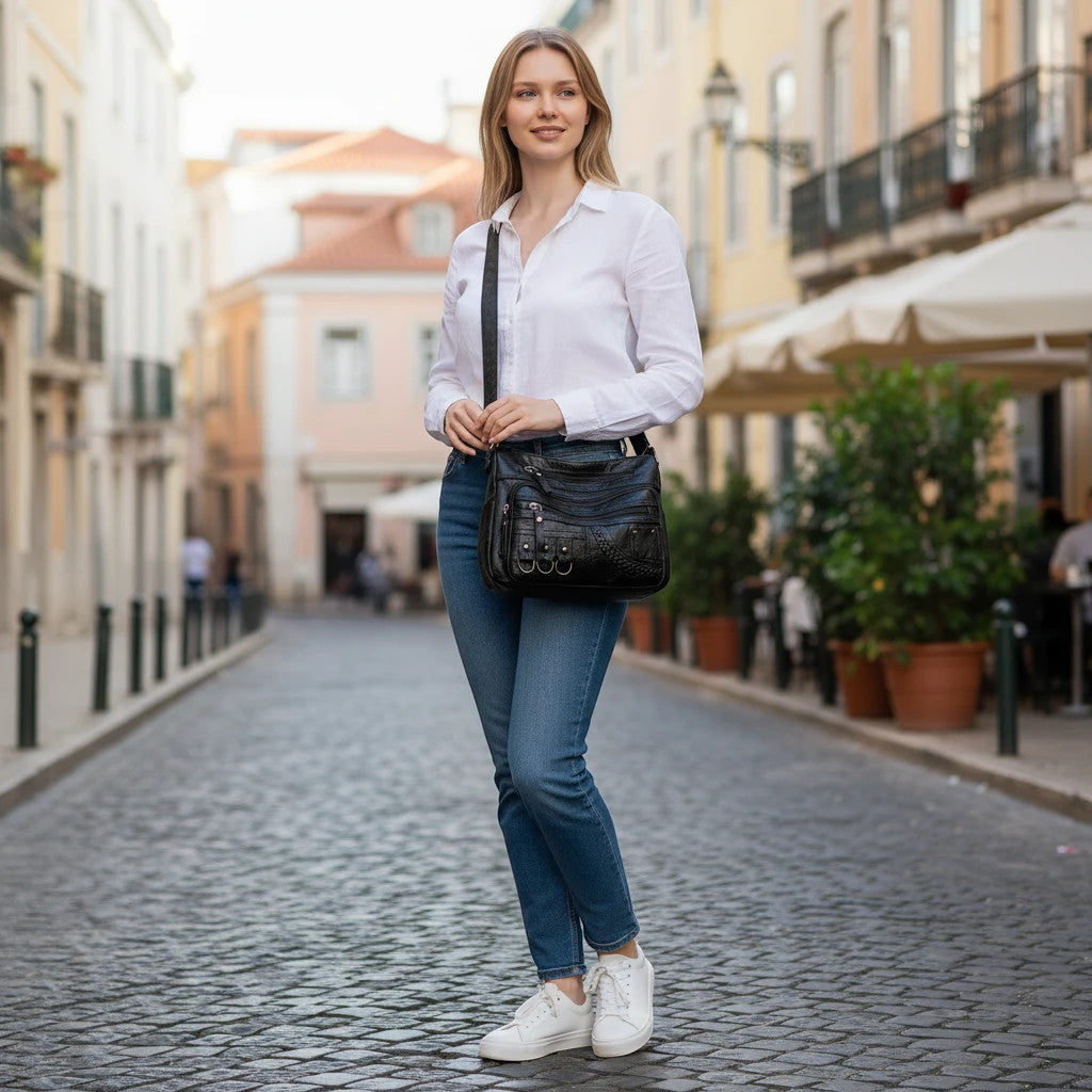 ZOFIA ATELIER Helena black PU leather crossbody bag with multiple pockets and silver hardware, worn by a woman in jeans and white shirt.