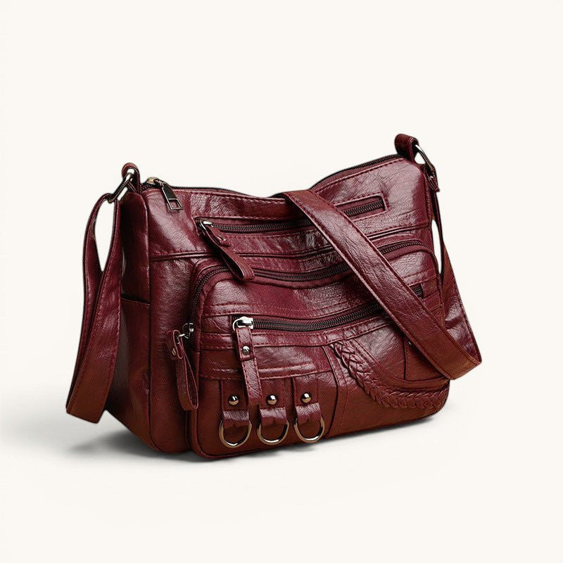 ZOFIA ATELIER Helena crossbody bag in burgundy PU leather with multiple zippered pockets and braided detail.