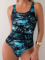 ZOFIA ATELIER Lidia one-piece swimsuit with a black and blue palm leaf print. Features a scoop neck and moderate leg cut.