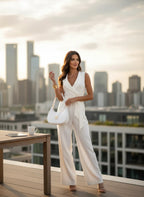 ZOFIA ATELIER sleeveless wide-leg white polyester jumpsuit with lapel collar and belt. Model wears it with a white handbag.