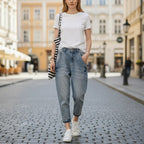 ZOFIA ATELIER light wash slim stretch cotton jeans with a tapered leg and cuffed hem, worn by a woman on a cobblestone street.