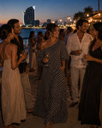 ZOFIA ATELIER black and white striped off-shoulder maxi dress with short sleeves and a flowing silhouette, worn by a woman at a beach party.