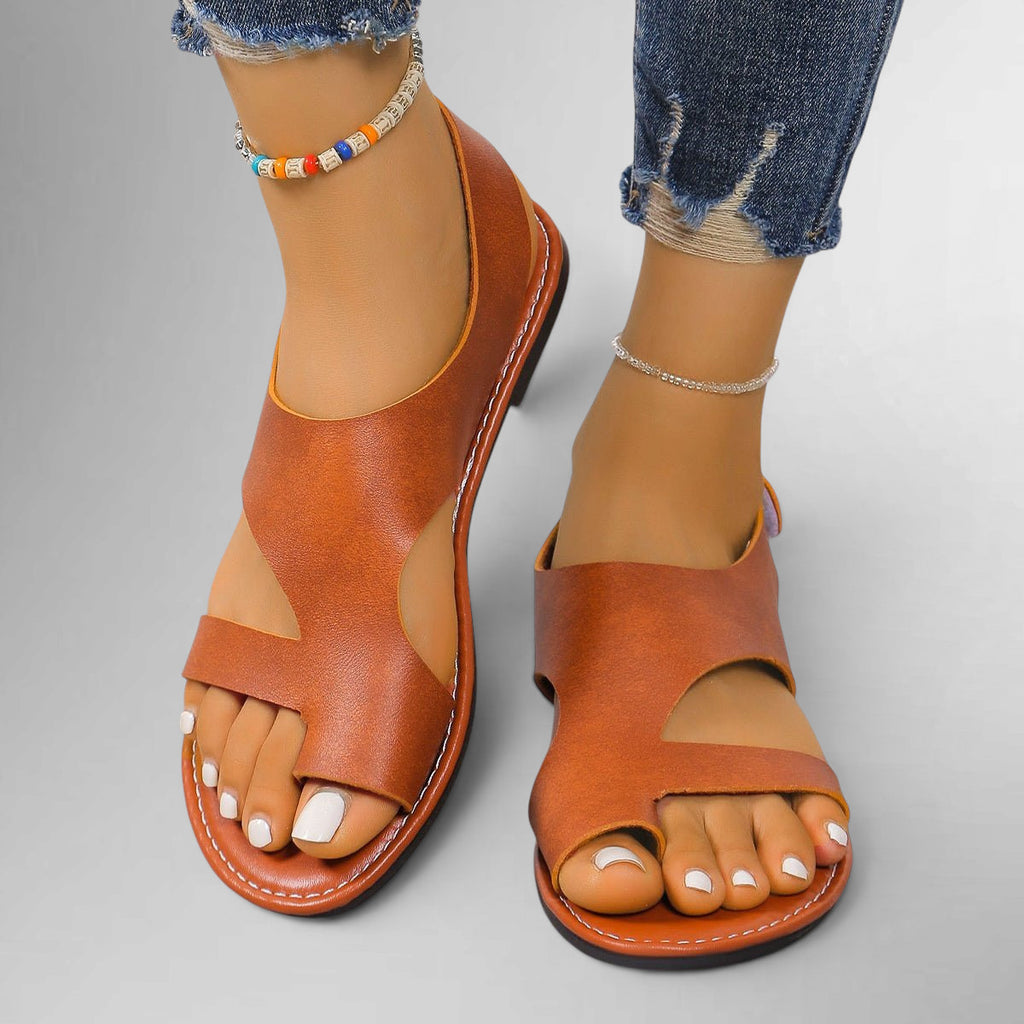 ZOFIA ATELIER tan leather flat sandals with velcro closure and open toe, white toenails, ankle bracelets, and distressed jeans.