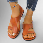 ZOFIA ATELIER tan leather flat sandals with velcro closure and open toe, white toenails, ankle bracelets, and distressed jeans.
