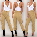 ZOFIA ATELIER tan slim-fit cargo overalls with high waist and zipper detail, paired with a white henley bodysuit and black heels.