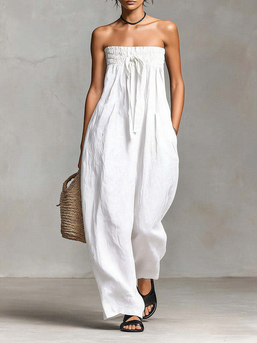 ZOFIA ATELIER white ruched strapless polyester jumpsuit with a drawstring waist and wide legs. Model is carrying a straw bag.